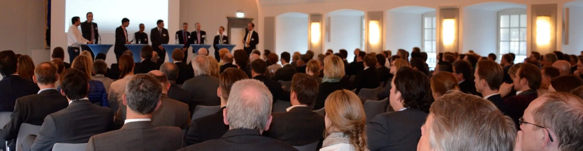 Schwarzweißfoto eines Mannes im Anzug, der am Rednerpult spricht und beide Hände ausdrucksvoll gestikulierend hebt