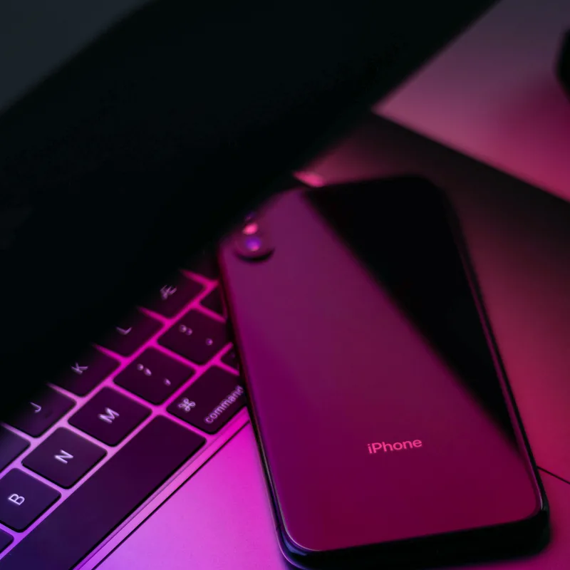 Smartphone auf neonbeleuchteter Laptop-Tastatur in Magenta-Licht, ZOOM-IN MWC 2019 Trendreport-Cover