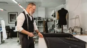 Master tailor measuring and cutting fabric at a workbench in a professional studio