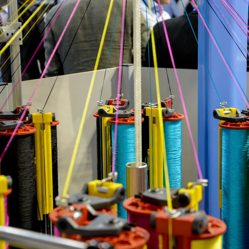 Nahaufnahme von industriellen Textilmaschinen mit bunten Garnspulen auf der Techtextil 2019 Frankfurt
