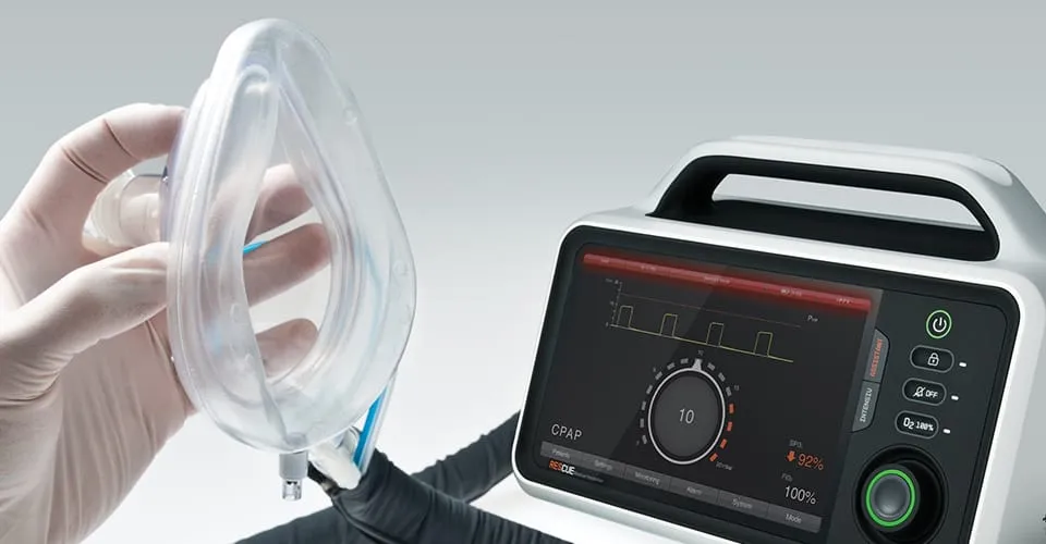 Behandschuhte Hände halten Atemmaske neben RESCUE-Beatmungsgerät mit CPAP-Modus auf dem Touchscreen