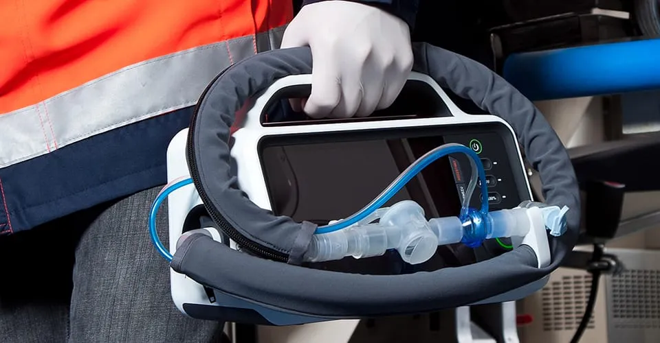 Sanitäter trägt RESCUE-Beatmungsgerät am Griff mit angeschlossenem Atemkreislauf im Rettungswagen