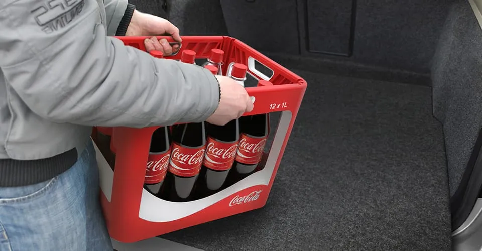 Person loading WAVE Coca-Cola multi-cycle crate into a car boot using rubberized grip handles