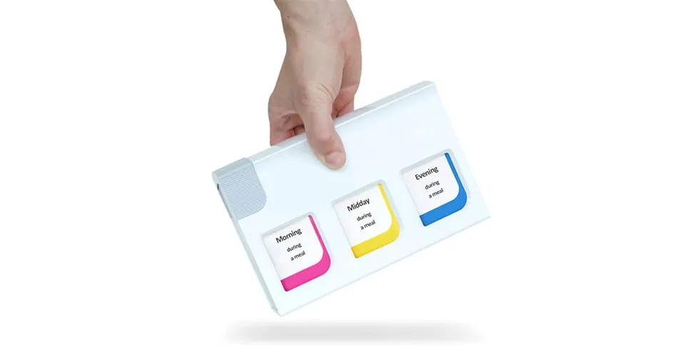Hand hält die weiße mediTimer-Einheit mit drei farbcodierten Fächern für Morgen, Mittag und Abend